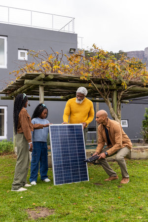 African American family with installer examining solar panel in backyard, senior in yellow sweater....