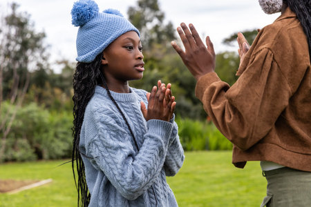 African-American parent-child clapping in park cable-sweater pom-beanie brown-jacket, copy space....
