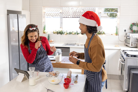 Couple Hispanic woman and African American man in aprons baking on kitchen island with glass bowl....