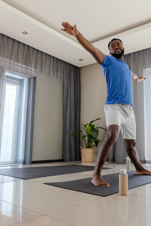African American man holding yoga pose on right mat wearing blue shirt gray shorts, copy space....