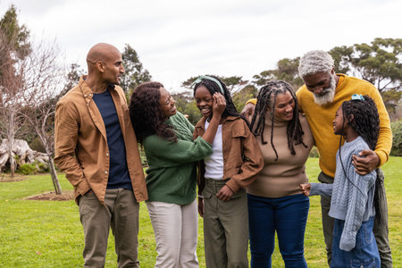 African American multigenerational family standing on grassy park lawn, wearing sweaters, smiling....
