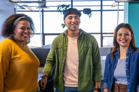 Diverse coworkers standing and smiling in modern office near grid windows with plants and chairs....
