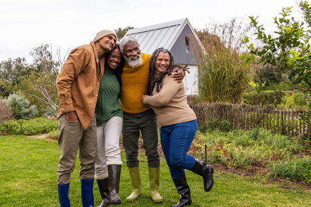 African American family standing arms linked on backyard lawn by shed, garden beds and rubber boots....