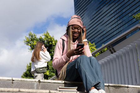 Diverse females with teen girl in pink hoodie sitting stone steps wearing headphones, holding phone....