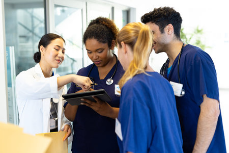 Four happy diverse healthcare colleagues looking at tablet together in hospital corridor. Hospital,...