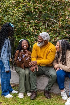 African American family sitting and standing on low wooden log in garden holding white flower....