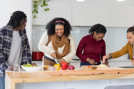 Diverse friends preparing meal, slicing yellow bell pepper with chef's knife on wooden island....