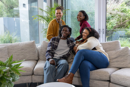 Diverse friends chatting while sitting on light gray sectional sofa near round white coffee table....