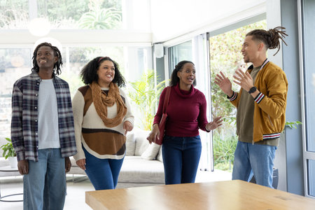 Diverse friends chatting and gesturing in modern living room near sofa and sliding glass doors....