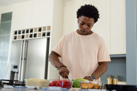 African American man chopping lettuce on cutting board at kitchen island, wearing smartwatch. Chef,...