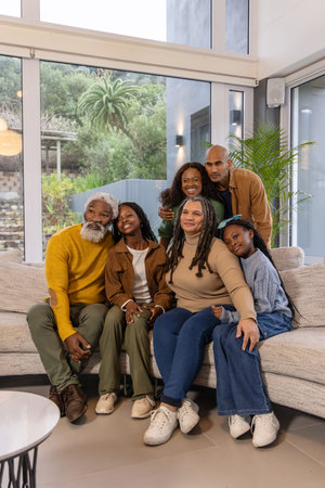 African American multigenerational family posing on light sectional sofa in modern living room....