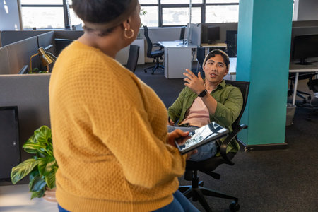 Diverse coworkers discussing project in open-plan office holding tablet near monitors, copy space....