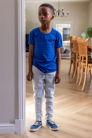 African American school-age boy standing in doorway at home wearing blue T-shirt and gray sweats....