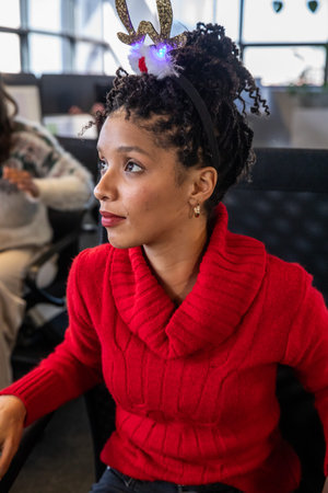 African American woman sitting in airport terminal wearing red sweater and LED antler headband....