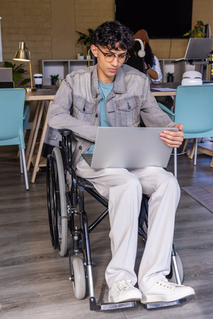 Diverse coworkers working in modern coworking space, man in wheelchair using silver laptop....