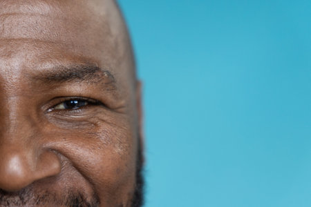 African American senior man smiling gently while posing in studio against turquoise backdrop. Closeup, portrait, headshot, cropped, background, bluegreen, cool