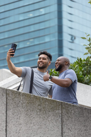 African American men taking selfie on concrete terrace leaning over barrier with smartphone. Urban, outdoor, greenery, smartwatch, casual, candid, friendship
