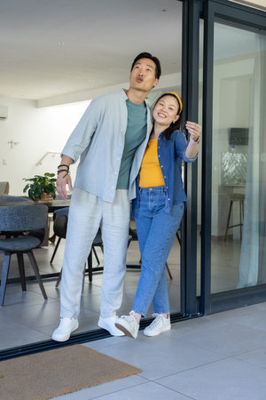 Asian couple standing at sliding glass door entry, woman leaning into man, pointing to doormat. Pair, contemporary, interior, openplan, threshold, kitchen, livingroom