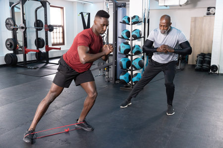 African American male trainer and client performing lateral step with red resistance band in gym