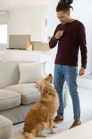 Standing man in maroon sweater looking down at sitting golden retriever in living room, copy space