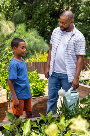 African American adult and youth males tending raised planter beds in yard with blue watering can