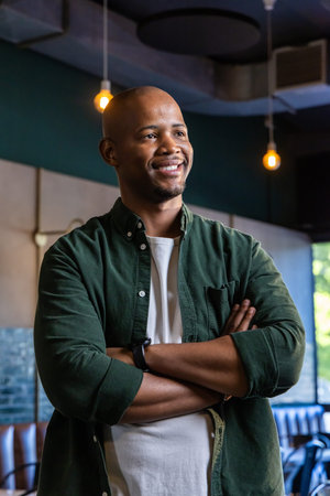 African American man in 30s standing with arms crossed, smiling at cafe with smartwatch, pendants