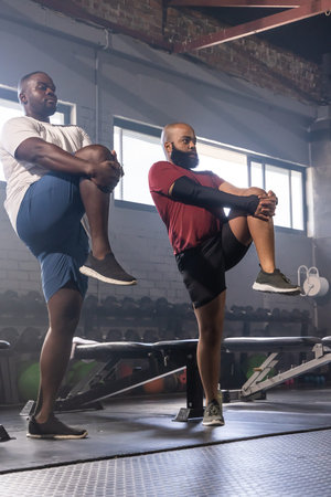 African American men doing single-leg stretches in gym with compression sleeve and kettlebells