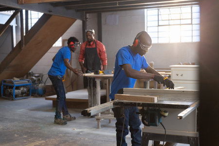 African American coworkers operating table saw assembling cabinets industrial workshop, copy space