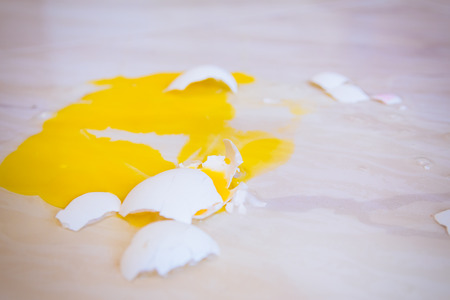 Close up of a broken egg that fell on the floor is splattered with yellow yolk everywhere.の写真素材