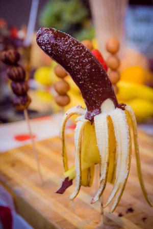 Banana on a stick coated chocolate with coconut chips and colored candies.Blur background.の写真素材