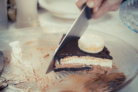 Female hand with a knife slicing chocolate-vanilla mousse cake with Glsaz of chocolate and white macaroon on it.の写真素材