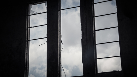 Broken window in an abandoned building - View from inside - sky with clouds seen through the windowの写真素材