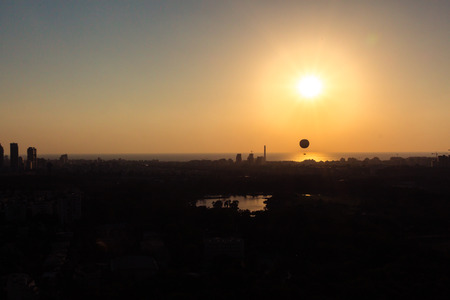 Tel Aviv skyline at sunset - silhouette. Can see a hot air balloon flying in the air. In addition, can see the neighborhood in north Tel Aviv, Hayarkon Park, Reading Power Station and the Mediterranean Sea.の写真素材