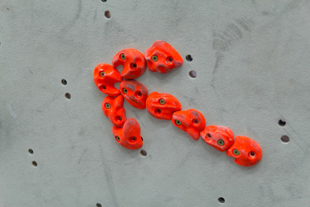 Red climbing holds in the shape of an arrow on grey wallの写真素材
