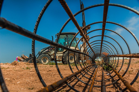 Workers and a tractor with a drilling device at a construction site - view from inside construction steel rod.の写真素材