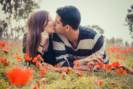 Young couple kissing while lying on the grass in a field of red poppies.の写真素材