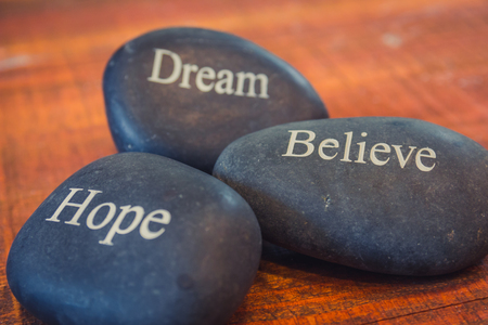 Black inspirational pebble stones with the words Dream, Believe and Hope on wooden background.の写真素材