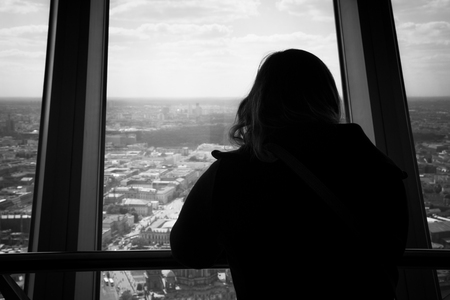 Silhouette of back view of woman looking out of a window at the berlin city skyline. View from inside of the tv tower building.の写真素材