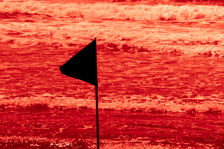 Black warning flag marking the limit of the safe swimming area at a beautiful beach with blue sky and a turquoise sea in israel. Red water horror concept.の写真素材
