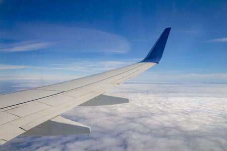Airplane wing on the sky and over sea with clouds.