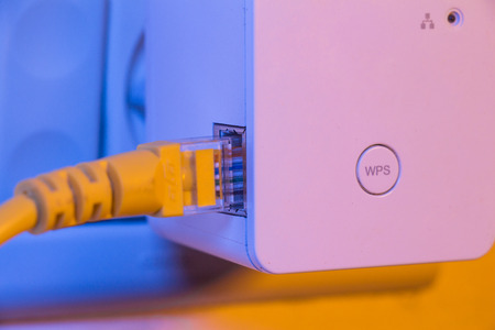 WiFi extender in electrical socket on the wall with a cable plugged in. The device is in access...