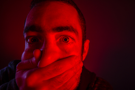 Closeup of a mans hand covering a man mouth with terrified facial expression.の写真素材