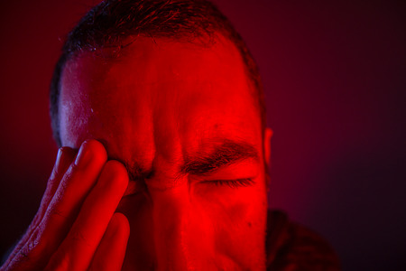Man is suffering in pain from headache. Close up headshot portrait of man feeling upset or in pain. He touches his head with his hand.の写真素材