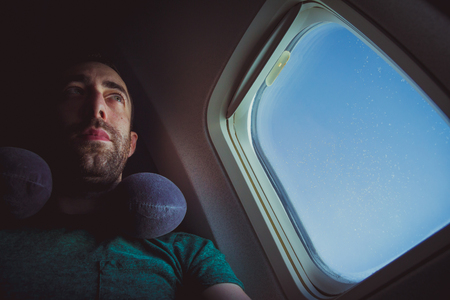Pensive man with neck pillow seat by the window of an airplane.の写真素材