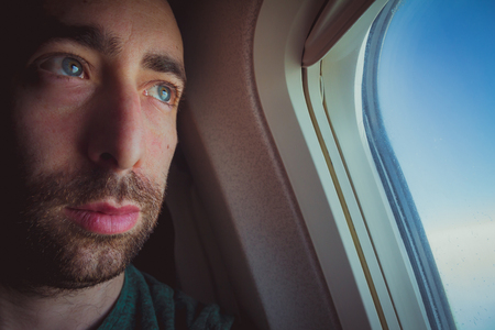 Close up of a pensive man looking outside through the window of an airplane.の写真素材
