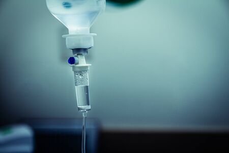 Set IV fluid intravenous drop saline drip in a hospital room. Close up, dark blue light background, selective focus and copy space.の写真素材