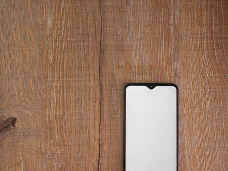 Black mobile smartphone mockup lies on the surface with blank screen isolated on wooden background....