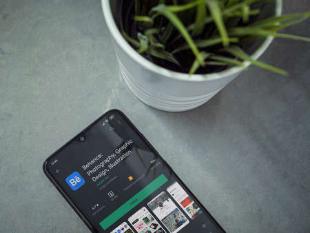 Lod, Israel - July 8, 2020: Modern minimalist office workspace with black mobile smartphone with Adobe Behance app play store page on a marble background. Close up top view flat lay.のeditorial素材