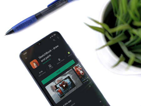 Lod, Israel - July 8, 2020: Modern minimalist office workspace with black mobile smartphone with Autodesk SketchBook app play store page on a white background. Close up top view flat lay.のeditorial素材