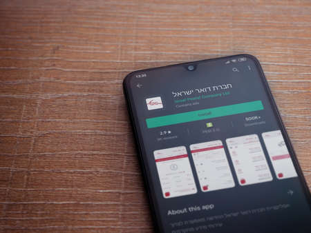 Lod, Israel - July 8, 2020: Israel Postal app play store page on the display of a black mobile smartphone on wooden background. Top view flat lay with copy space.のeditorial素材